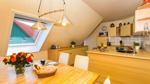 Una cucina con un tavolo di legno, sedie, un vaso di fiori e una finestra vista su un edificio con il tetto rosso.