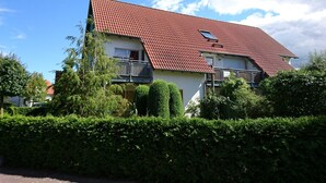 Un edificio residenziale a due piani con tetto in tegole rosse, un balcone al secondo piano e una piccola finestra al terzo piano.