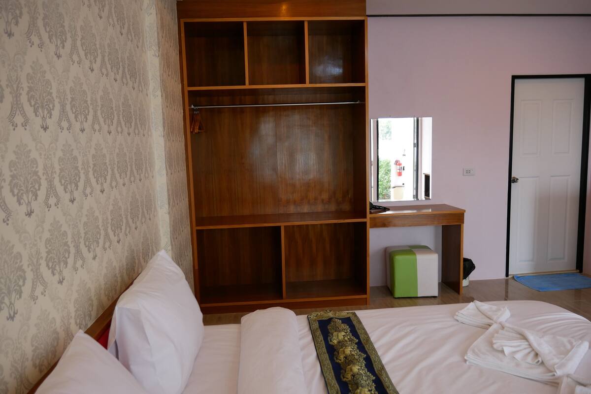 A hotel room with a bed, a wooden wardrobe, a desk with a mirror, and a door.