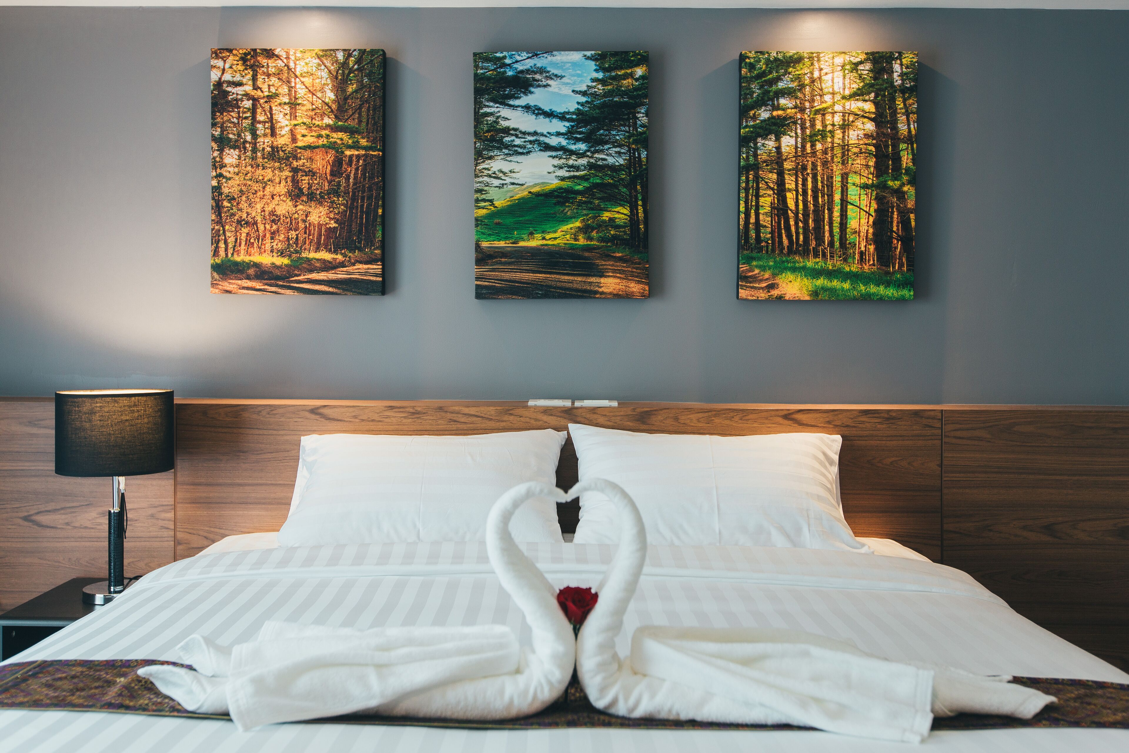 Una habitación de hotel con una cama, una mesita de noche y tres cuadros enmarcados con paisajes boscosos en la pared.