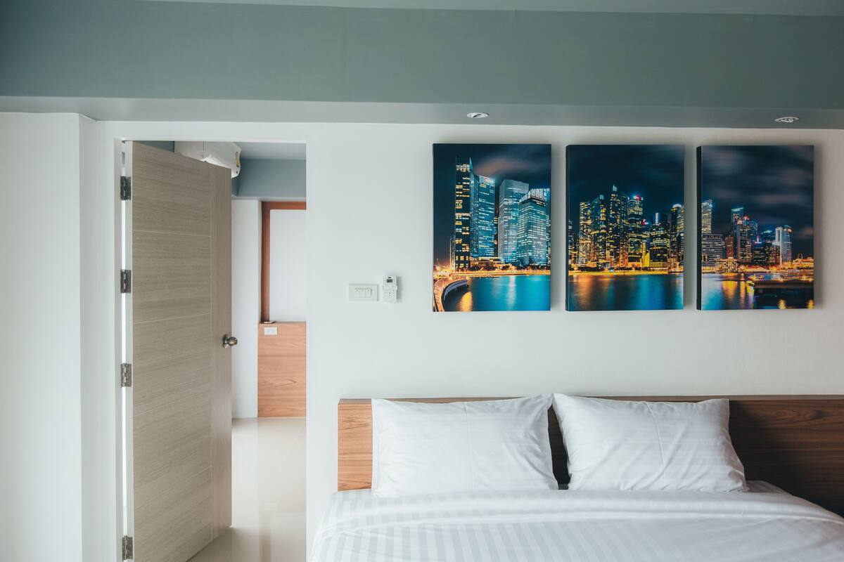 A hotel room with a bed, a cityscape artwork on the wall, and a wooden door.