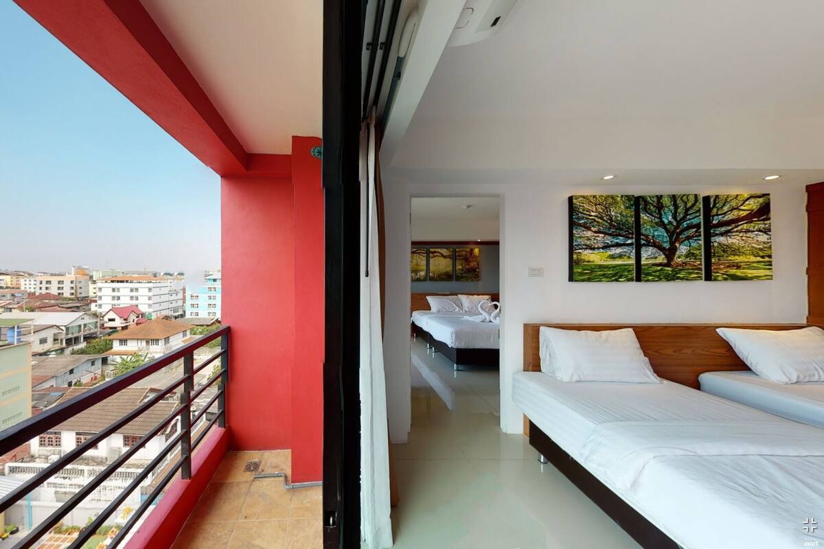 A hotel room with a balcony, a bed, a painting, and a view of the cityscape.