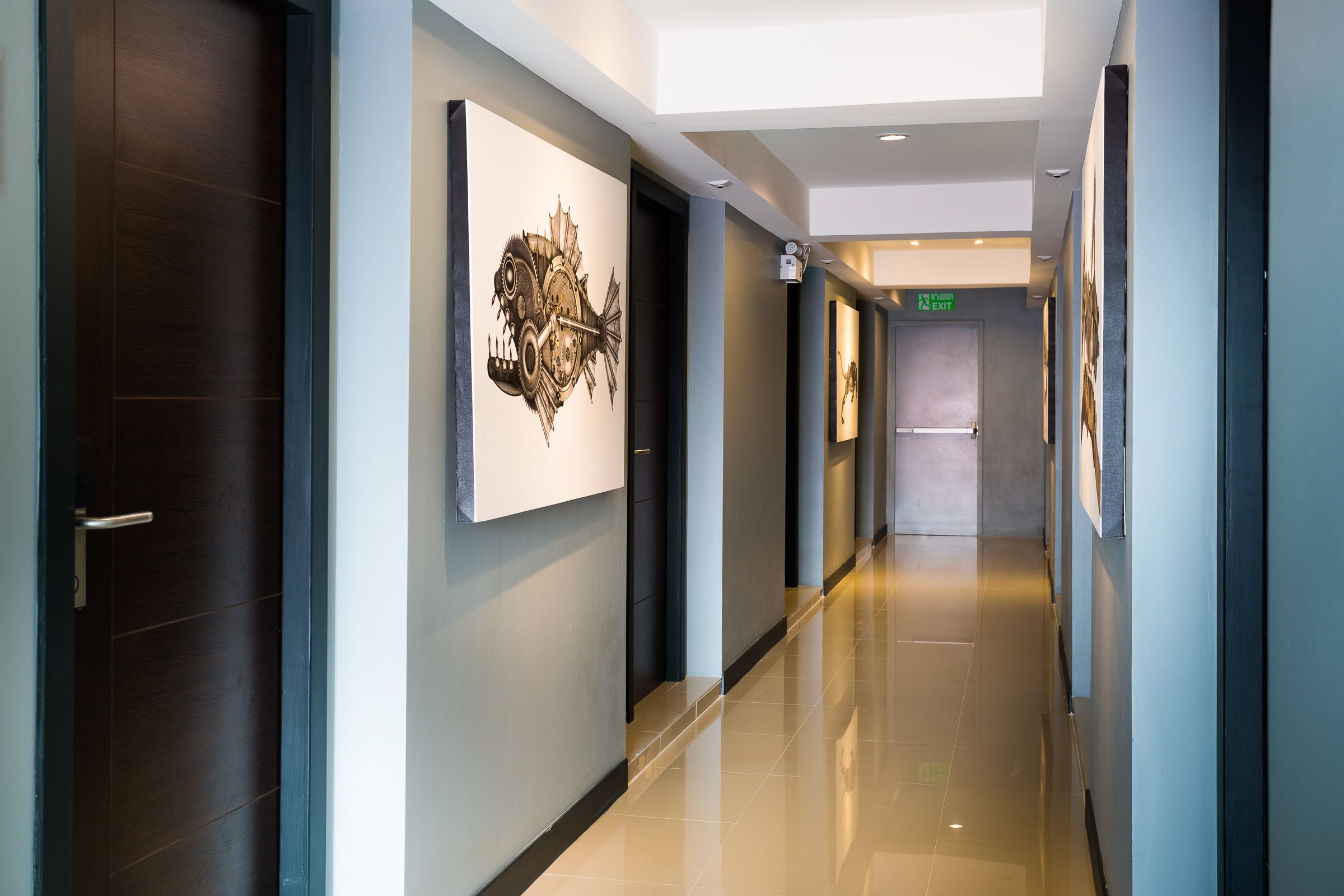 A modern hotel corridor with a polished floor, a large abstract artwork on the wall, and an exit sign.