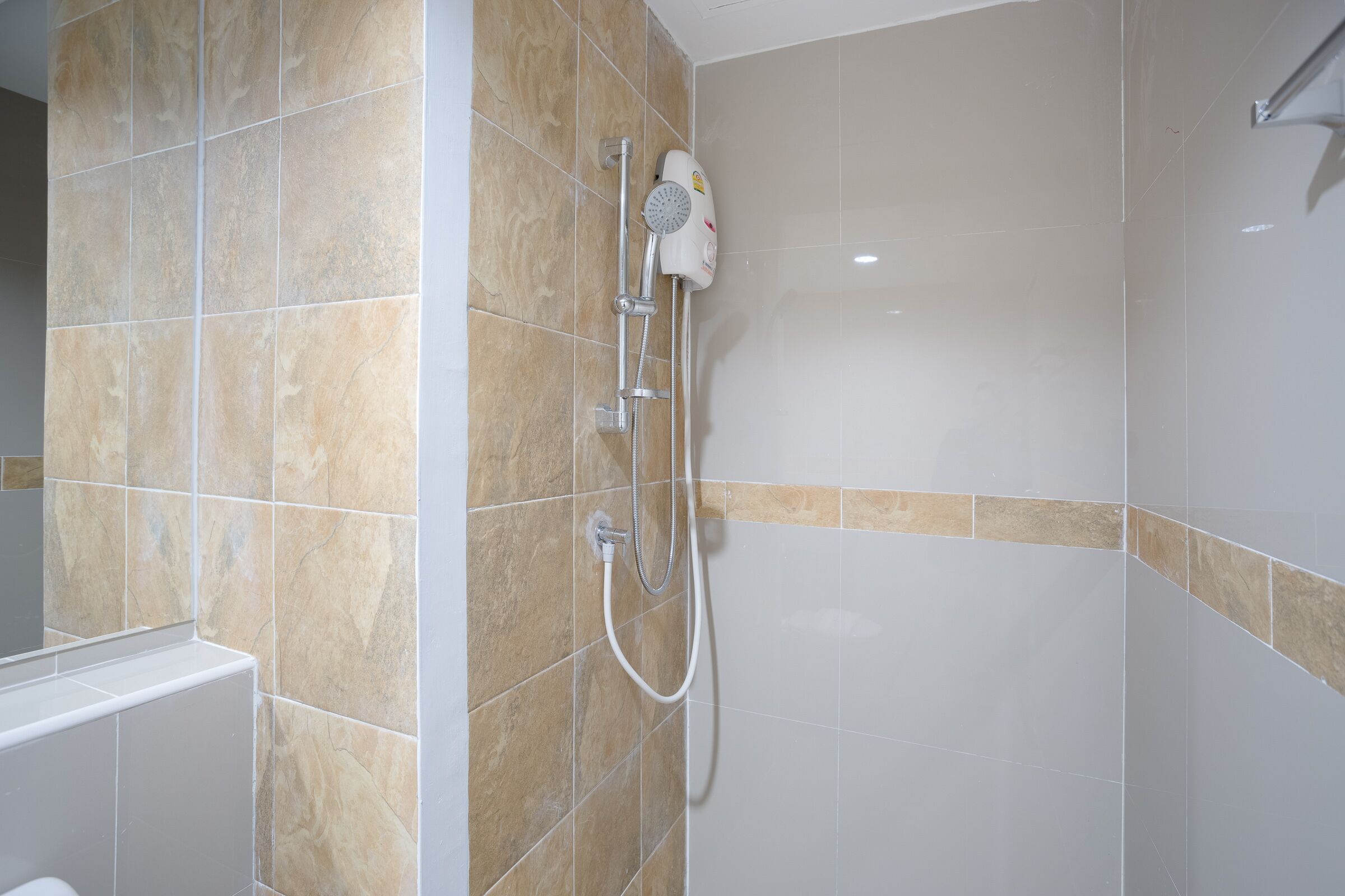 Un baño con azulejos beige y blancos, un cabezal de ducha y un accesorio de ducha de mano.