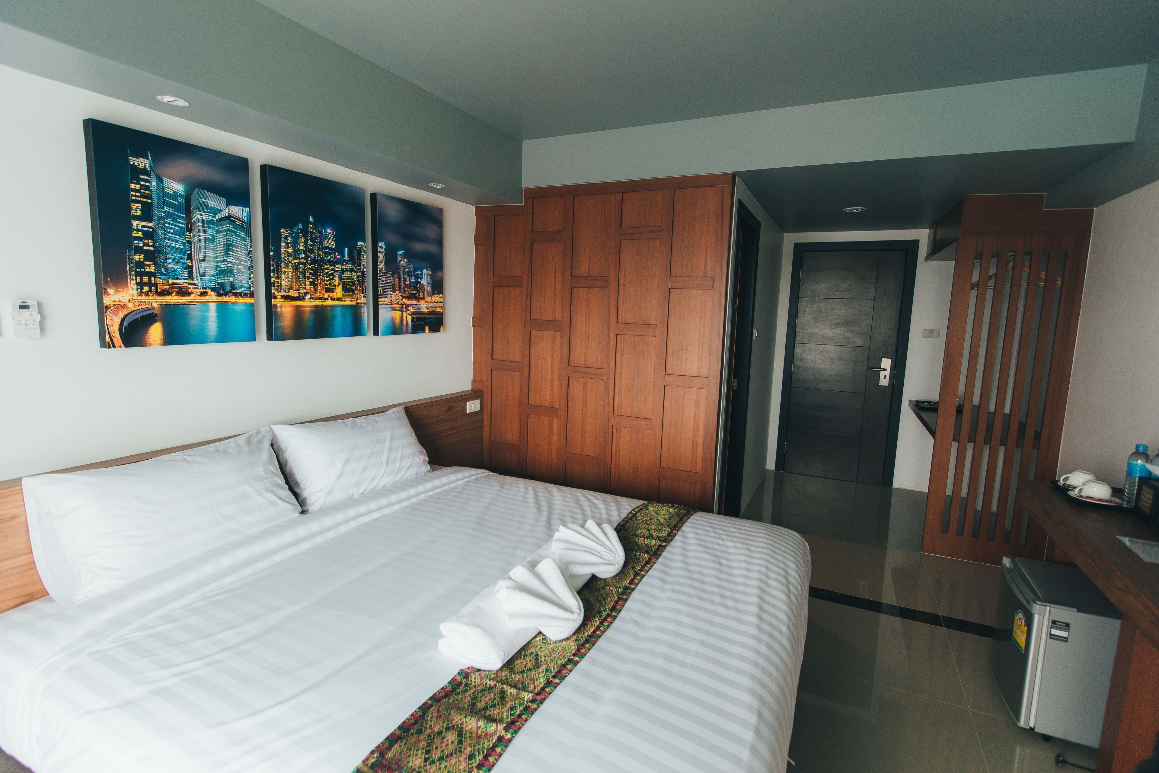 A hotel room with a large bed, wooden wardrobe, and a cityscape view.