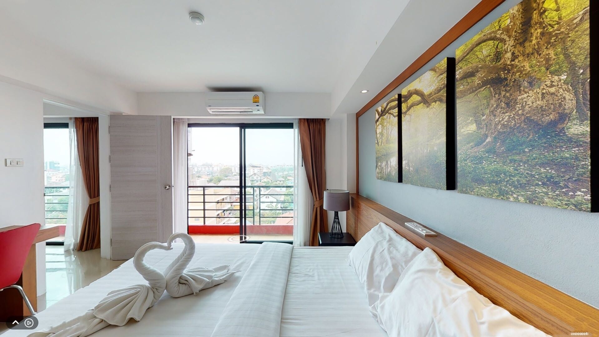 Una habitación de hotel con cama, un cuadro, una lámpara y vista a la ciudad por la ventana.