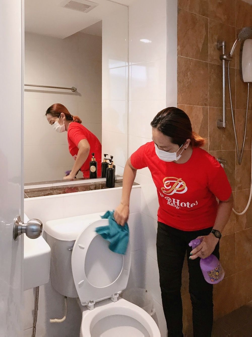 Una persona limpiando un baño con inodoro, lavabo y espejo.