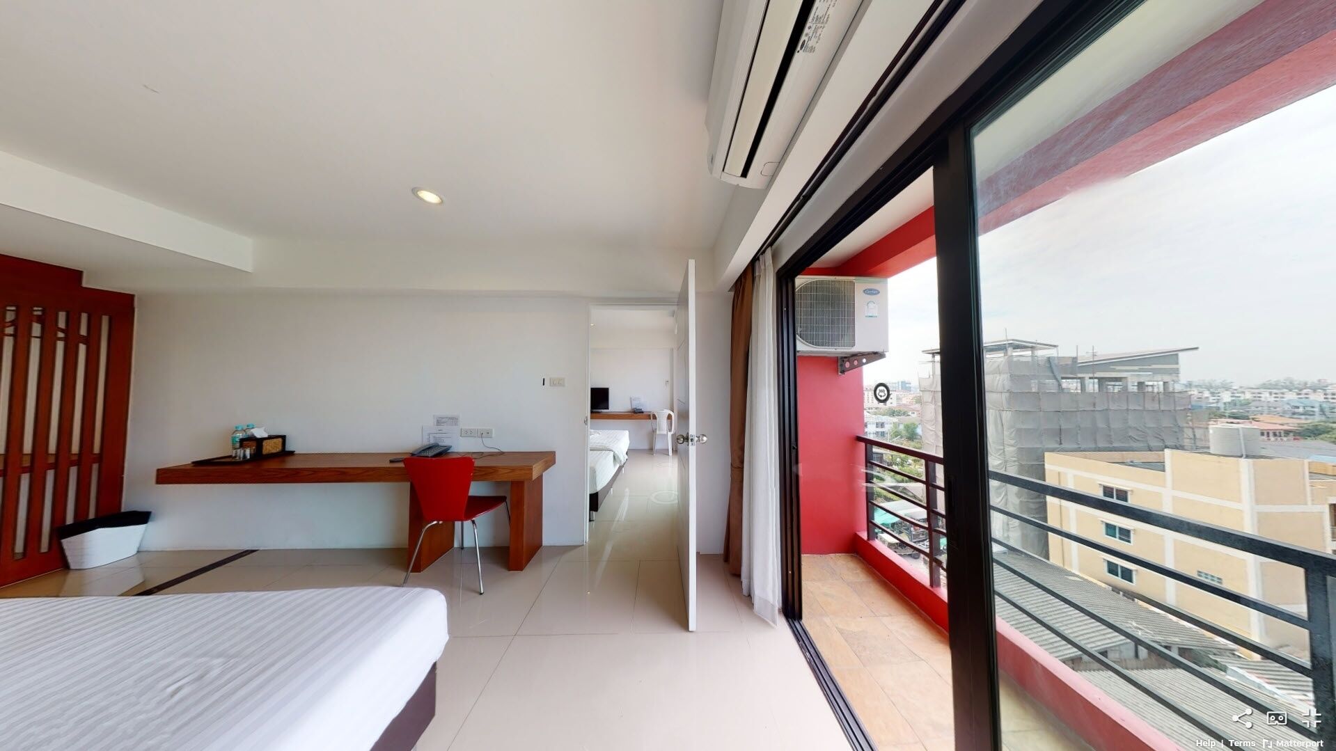 A modern hotel room with a bed, a desk, and a balcony with a city view.