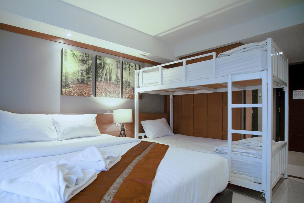 A hotel room with a bunk bed, a single bed, and a large window with a forest view.