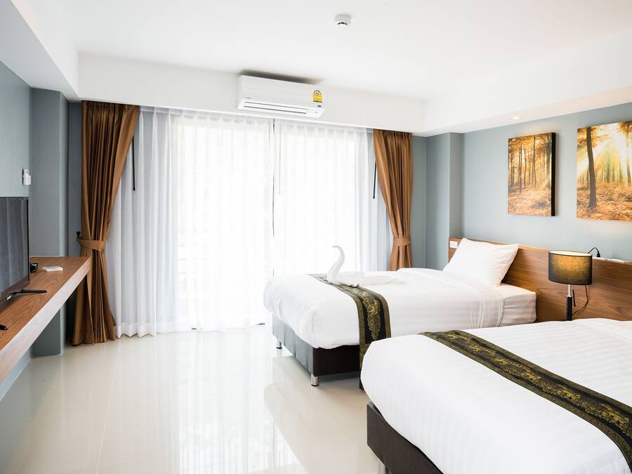 A hotel room with two beds, a desk with a TV, and a large window with curtains.