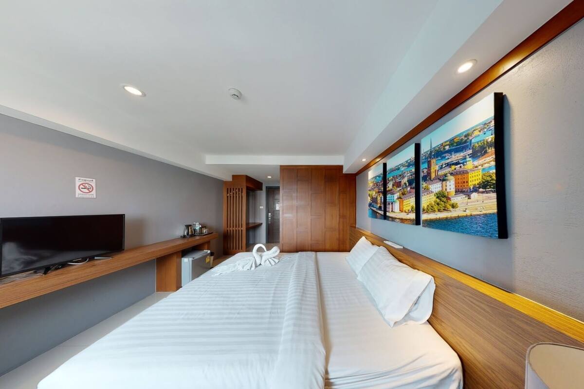 A modern hotel room with a large bed, a TV, a desk with a computer, and a painting of a cityscape.