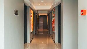 Un couloir d’hôtel moderne, avec un sol brillant, des murs sombres et des œuvres d’art colorées qui les décorent.