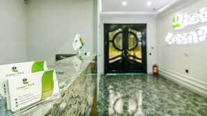 Zona de recepción de un hotel con un mostrador de mármol, un cartel del hotel en color verde y una puerta negra con diseño circular.