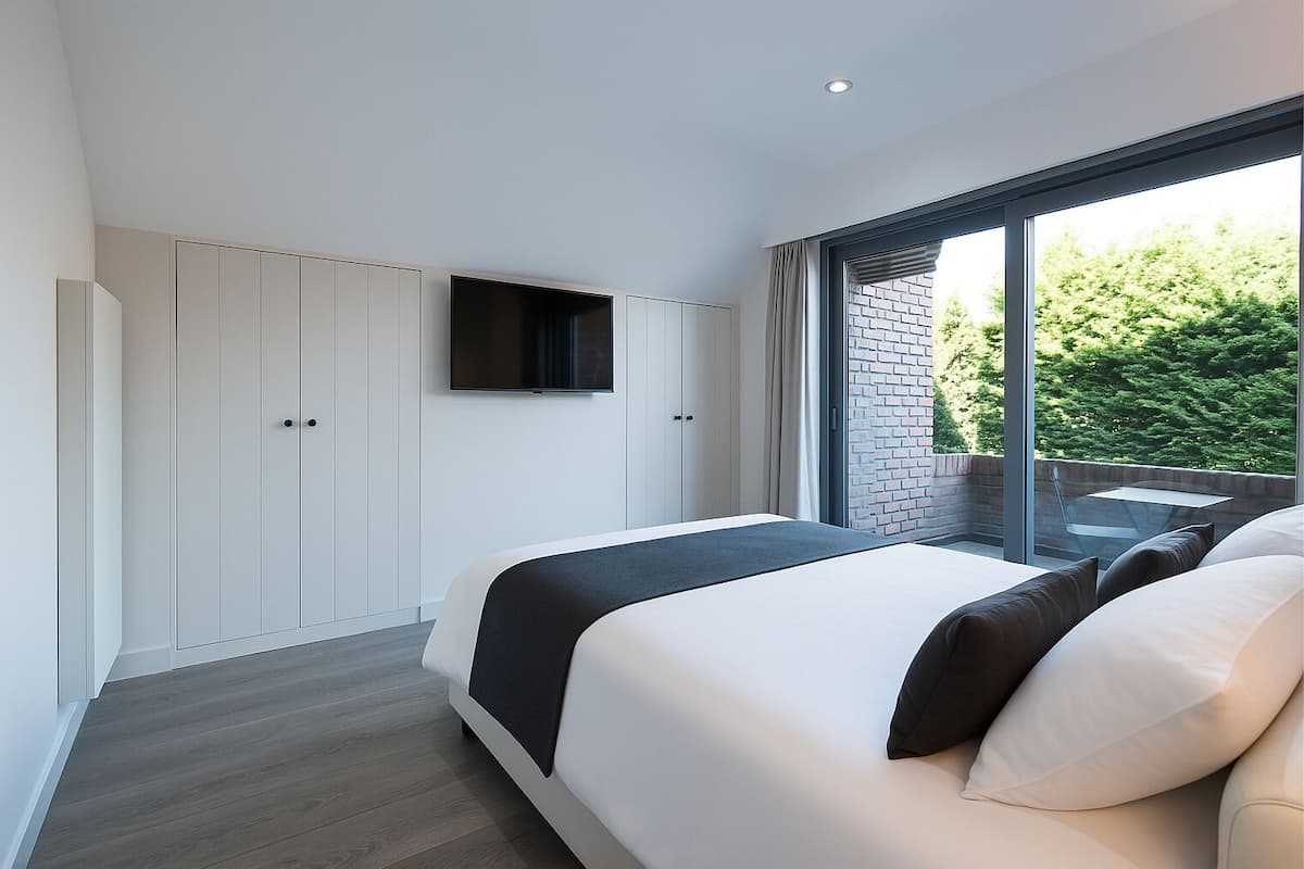 Quarto moderno com uma cama grande, televisão de tela plana na parede e uma janela ampla com vista para o verde.
