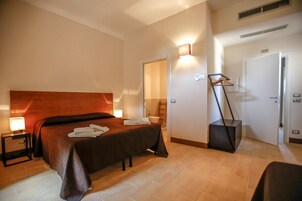Una habitación de hotel con una cama grande, una mesita de noche con lámpara, un armario y un baño visible a través de una puerta abierta.
