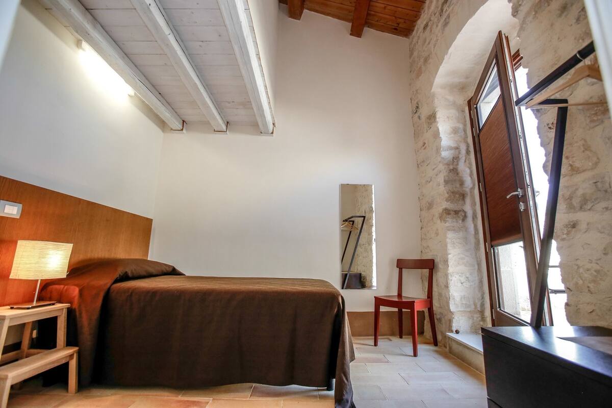 A bedroom with a bed, a desk, a chair, and a window.