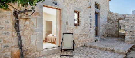 A stone building with a tiled patio, a hanging chair, and a vine growing on the wall.