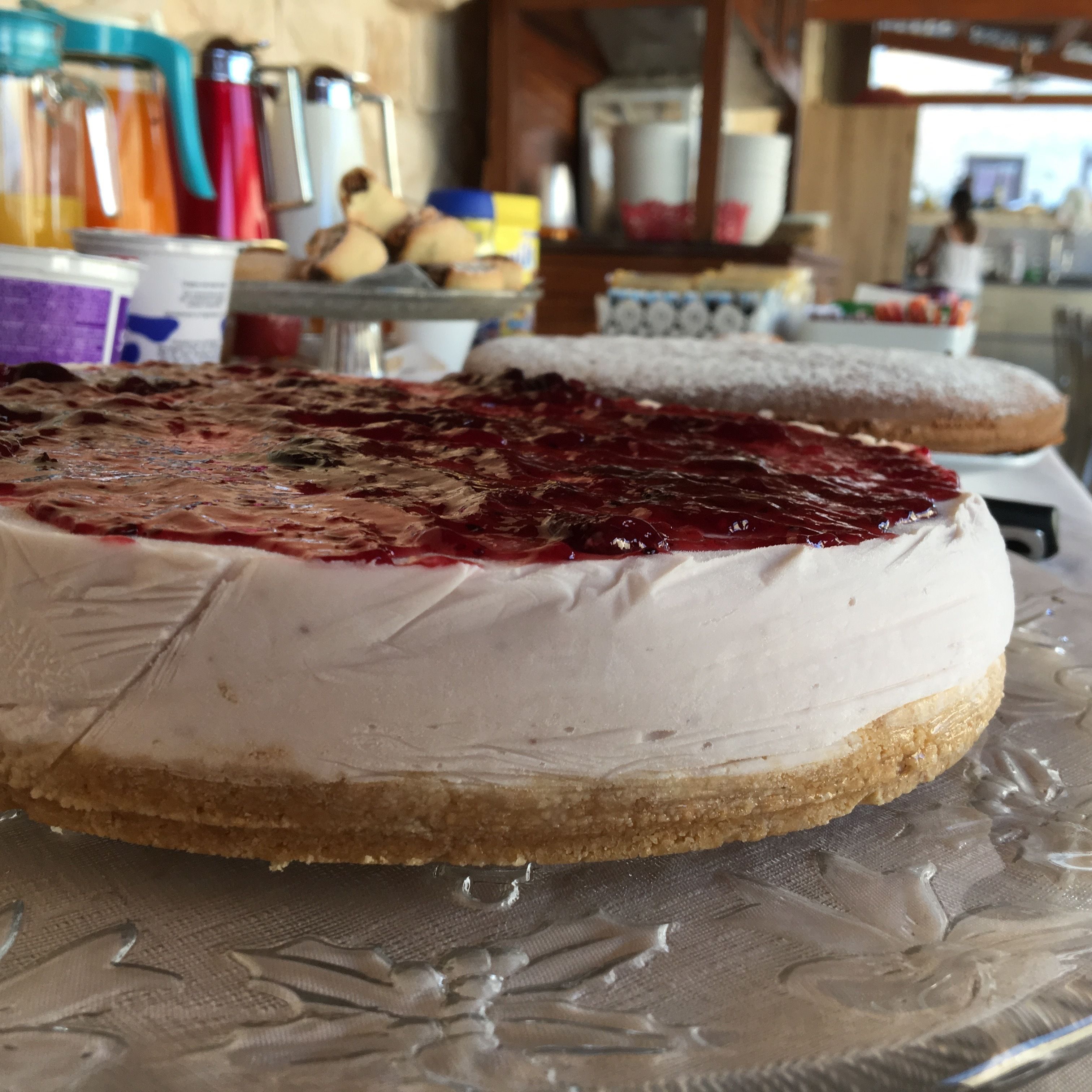 Un pastel redondo con cobertura blanca y una capa de fruta roja sobre un plato de vidrio.