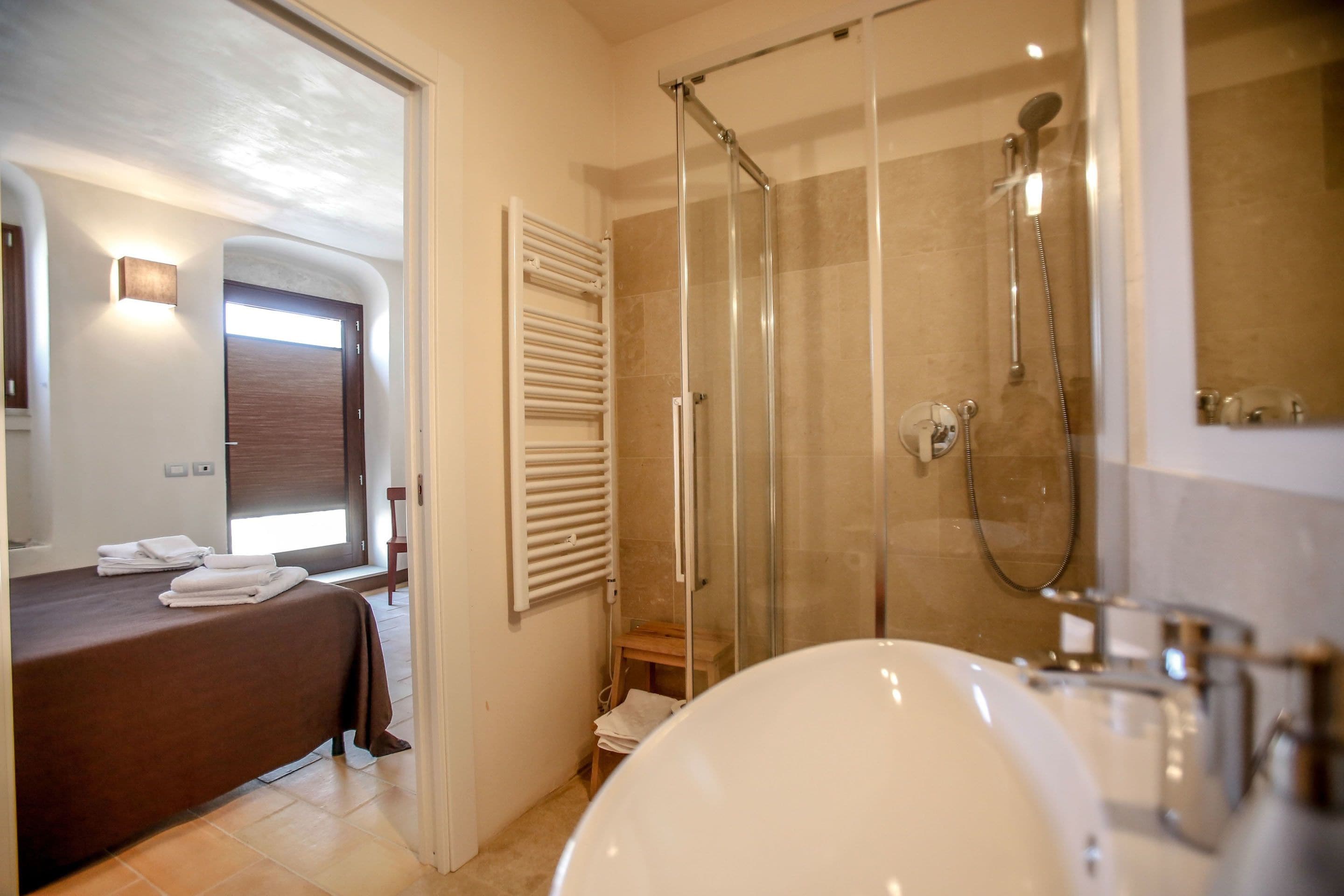 A modern bathroom with a glass-enclosed shower, a large white sink, and a bed with towels.