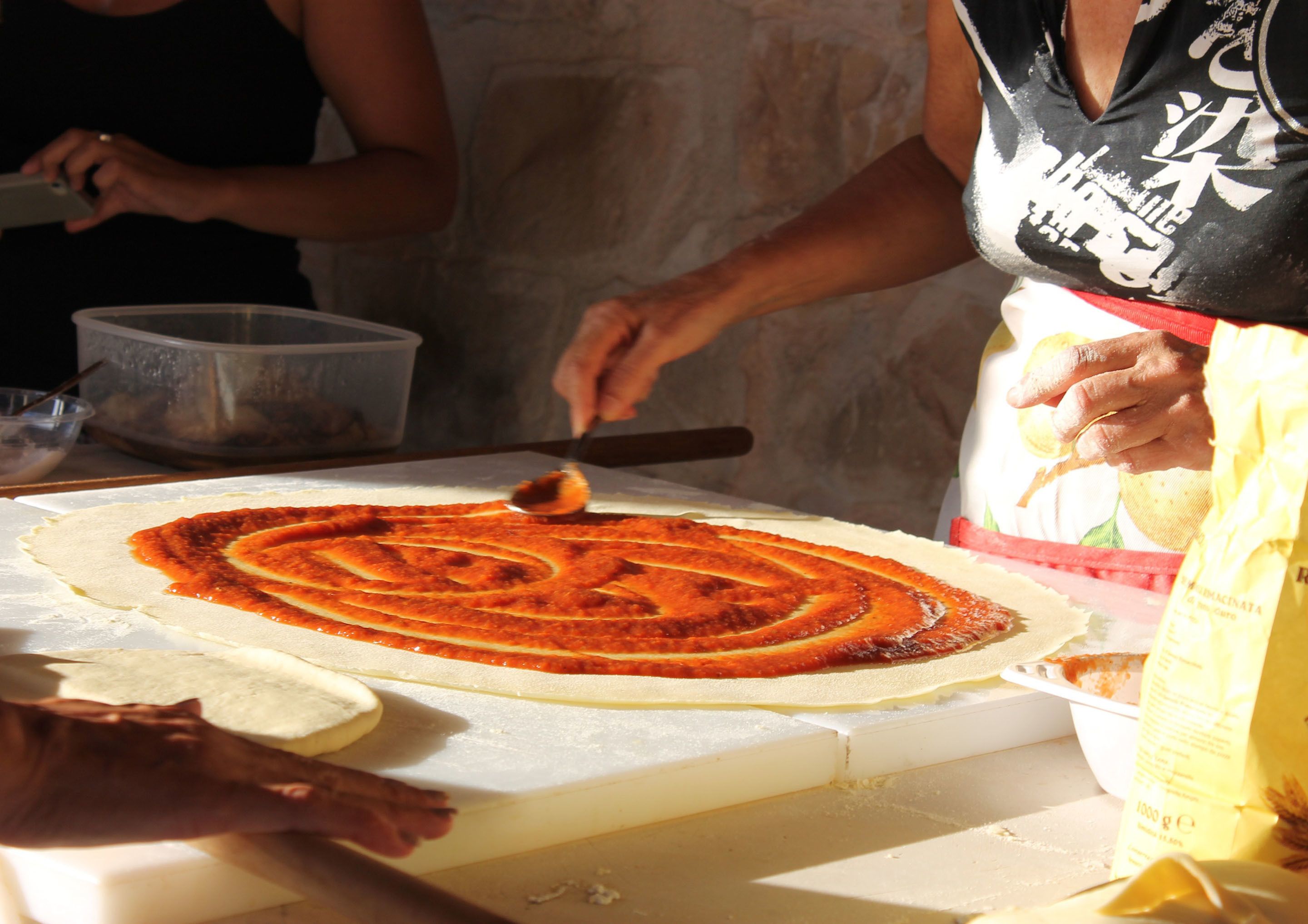 Una persona prepara una pizza su un tavolo, usando un matterello e una pala per pizza.