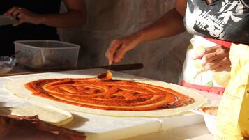 Una persona prepara una pizza su un tavolo, usando un matterello e una pala per pizza.