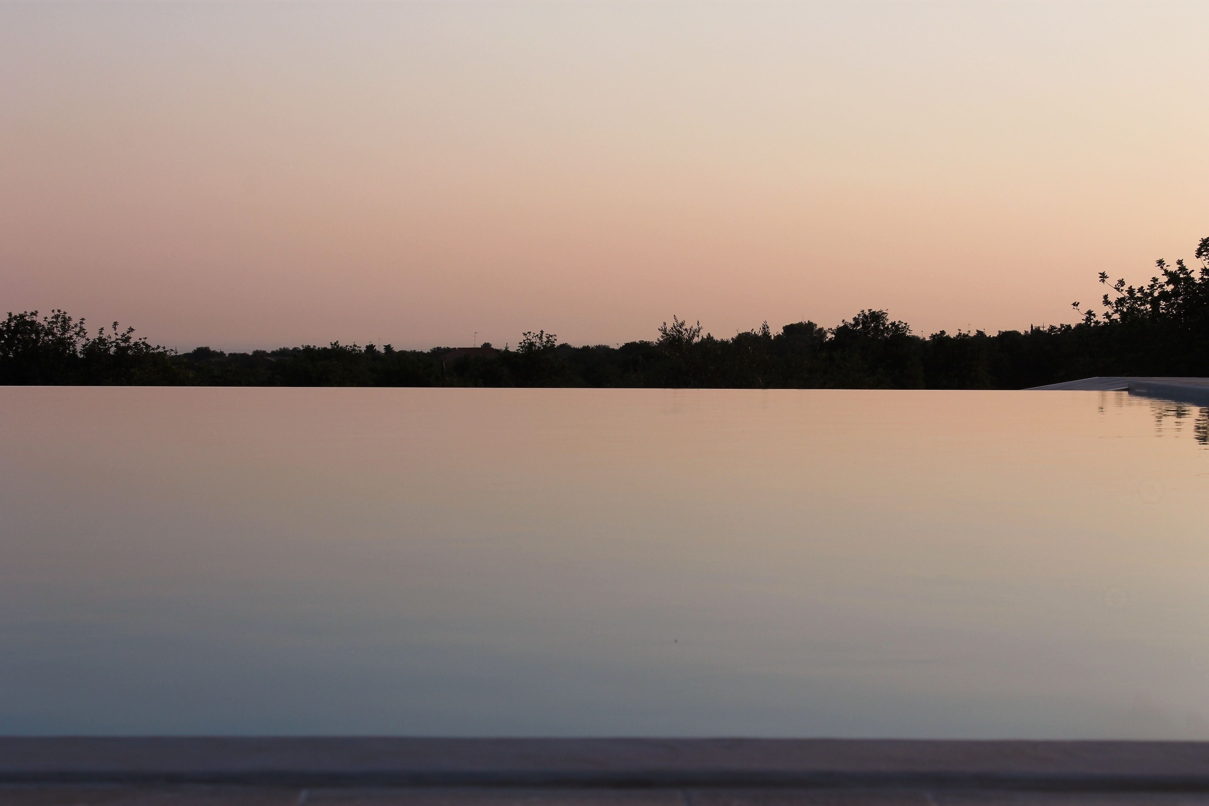 A tranquil outdoor pool area with a clear view of the horizon and a line of trees in the background.