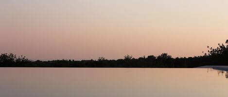 A tranquil outdoor pool area with a clear view of the horizon and a line of trees in the background.