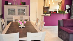 A dining area with a wooden table and white chairs, a kitchen with purple walls, and a grey sofa. - House in Touraine with Spa and Sauna, near Loire Castles (Benais)