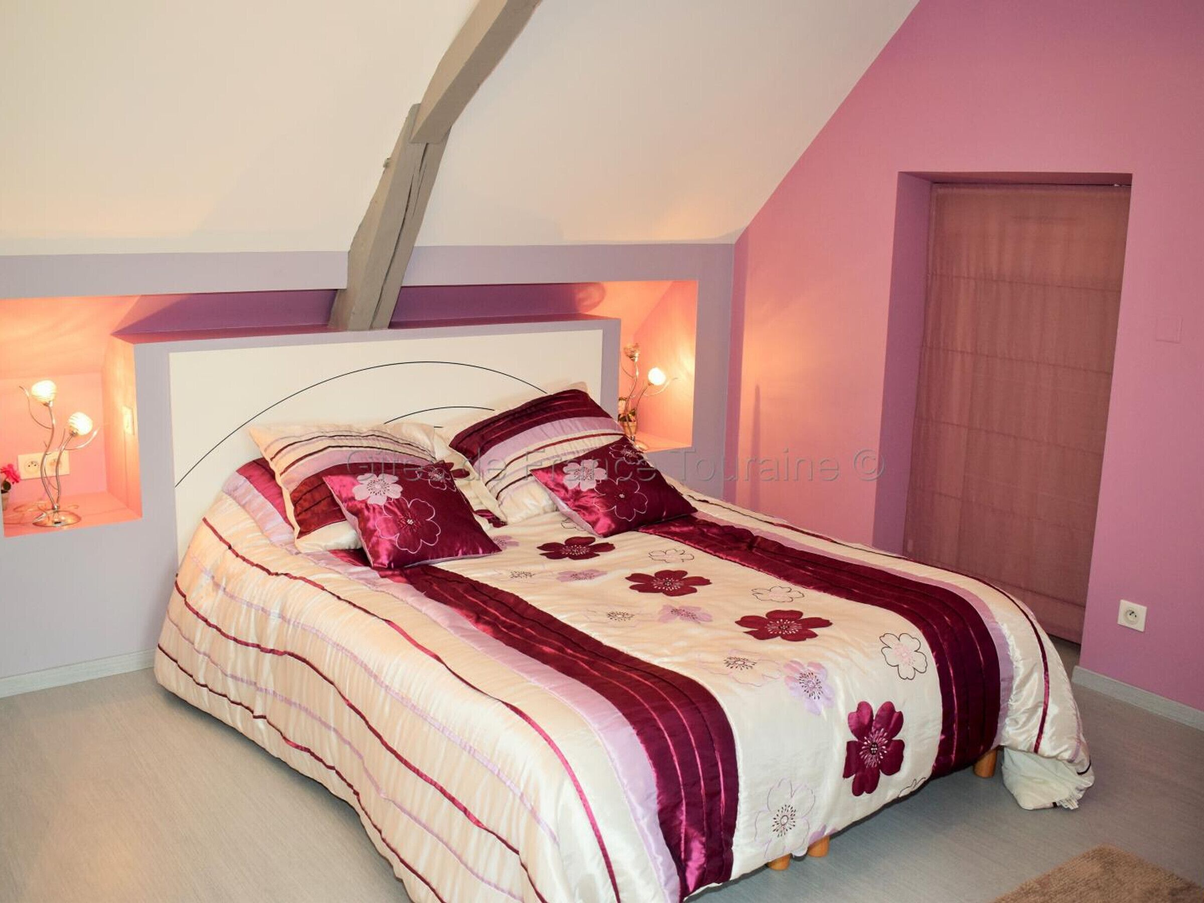 Een slaapkamer met een bed, hoofdbord, een wandlamp en een deur.