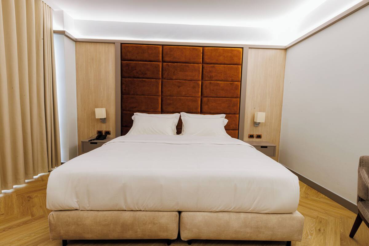 A large bed with a wooden headboard, two bedside tables, and a chair.