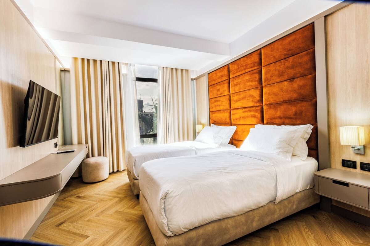 A modern hotel room with two beds, a TV, and a wooden headboard.