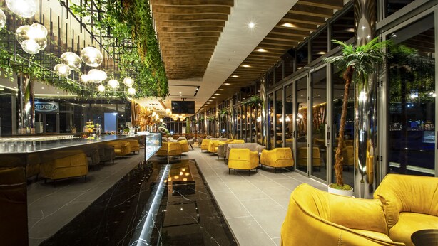 Eine moderne Bar mit Marmorboden, gelben Sitzgelegenheiten und einer grünen Wand mit hängenden Pflanzen.