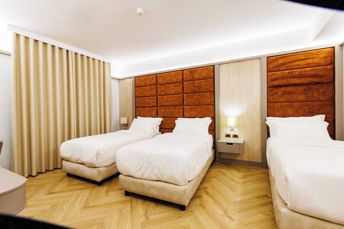 A hotel room with two beds, wooden flooring, and a modern design.