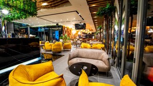 Ein stilvoller Lounge-Bereich mit gelben Sitzgelegenheiten, einem Fernseher und einer Bar mit einer Neonreklame.