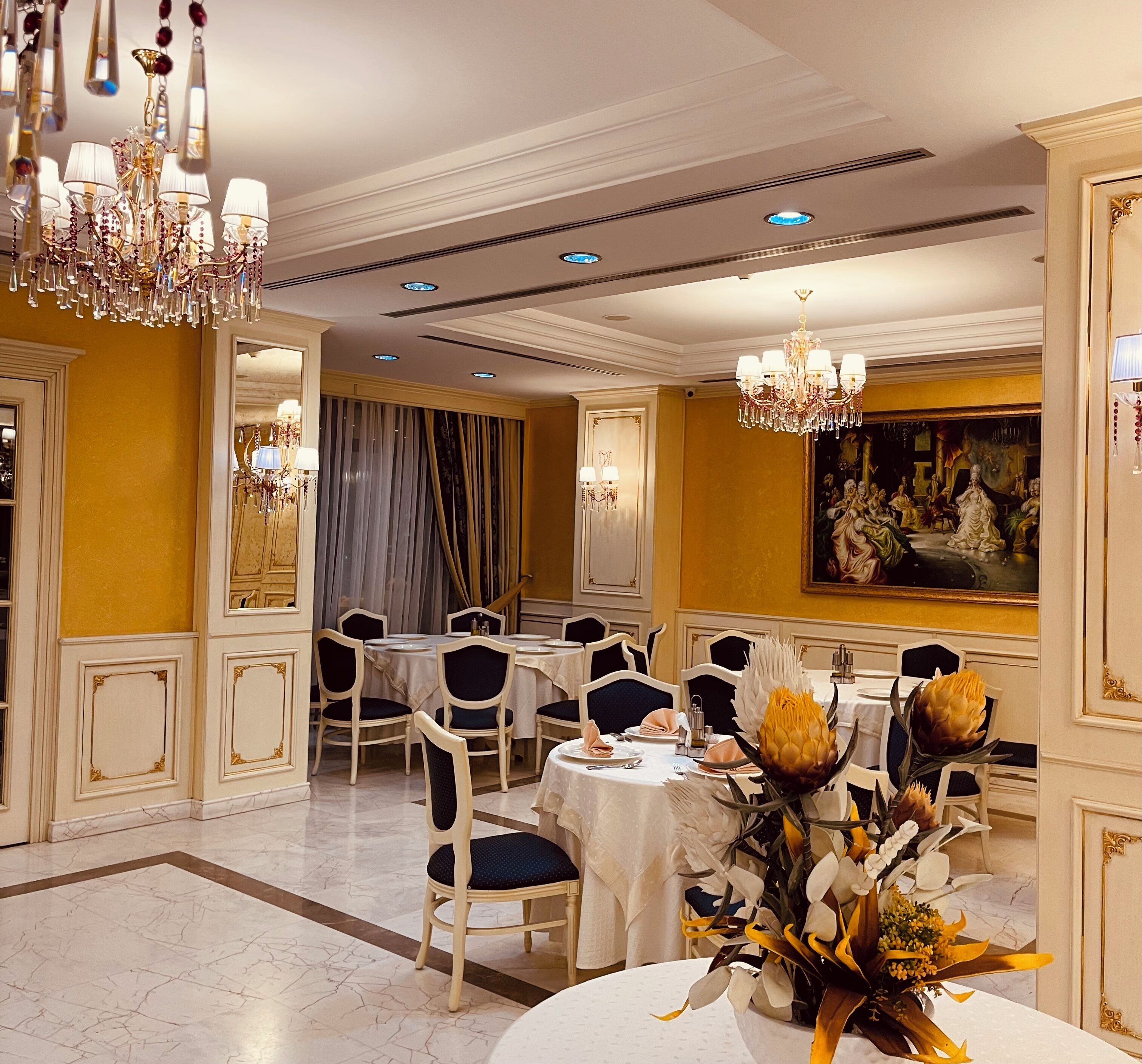 A formal dining room with chandeliers, white tablecloths, and classic chairs.