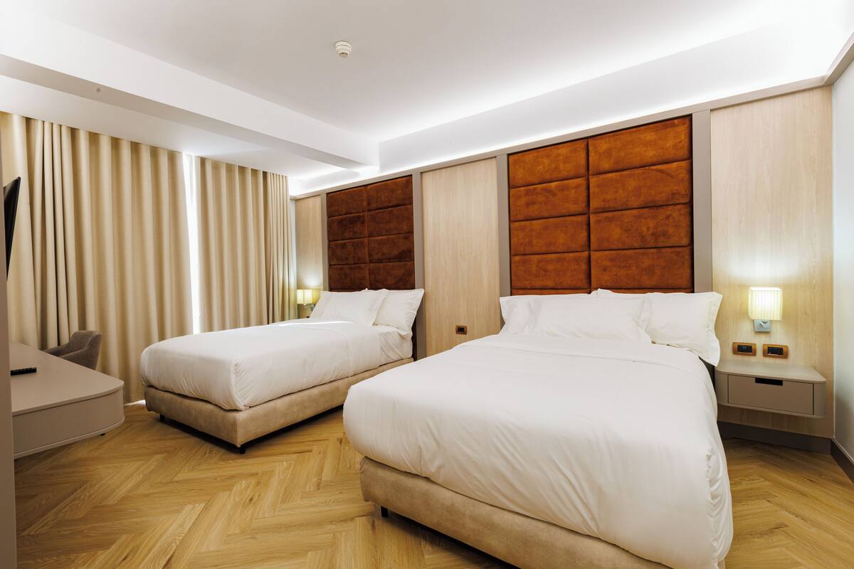 A hotel room with two beds, a desk, and a TV.
