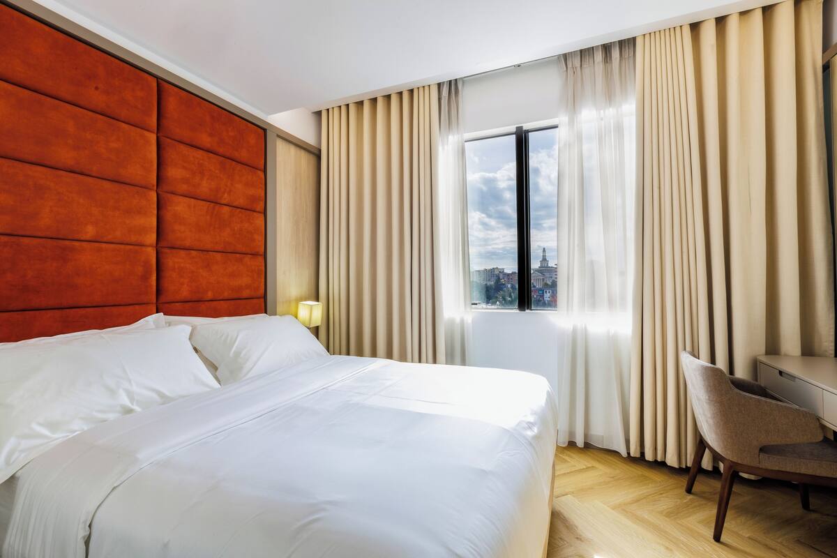 A hotel room with a large bed, a desk, and a window with curtains.