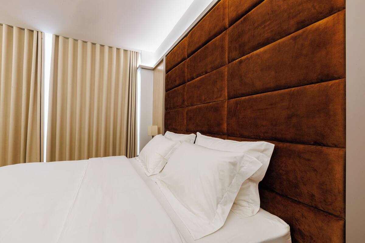 A hotel room with a large bed, beige curtains, and a wooden headboard.
