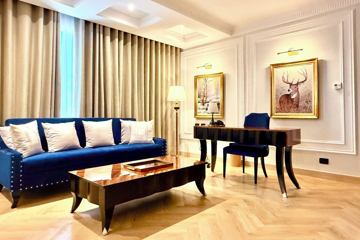 A modern living room with a blue sofa, a wooden coffee table, a piano, and two framed deer paintings on the wall.