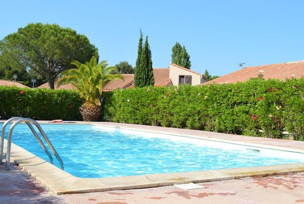 Relax by the clear blue pool surrounded by lush greenery and a Mediterranean-style backdrop.
