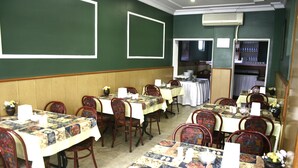 A dining area with multiple tables and chairs, some with tablecloths. There are wall-mounted air conditioning units and a shelf with bottles. - Acikgoz Hotel (Edirne)