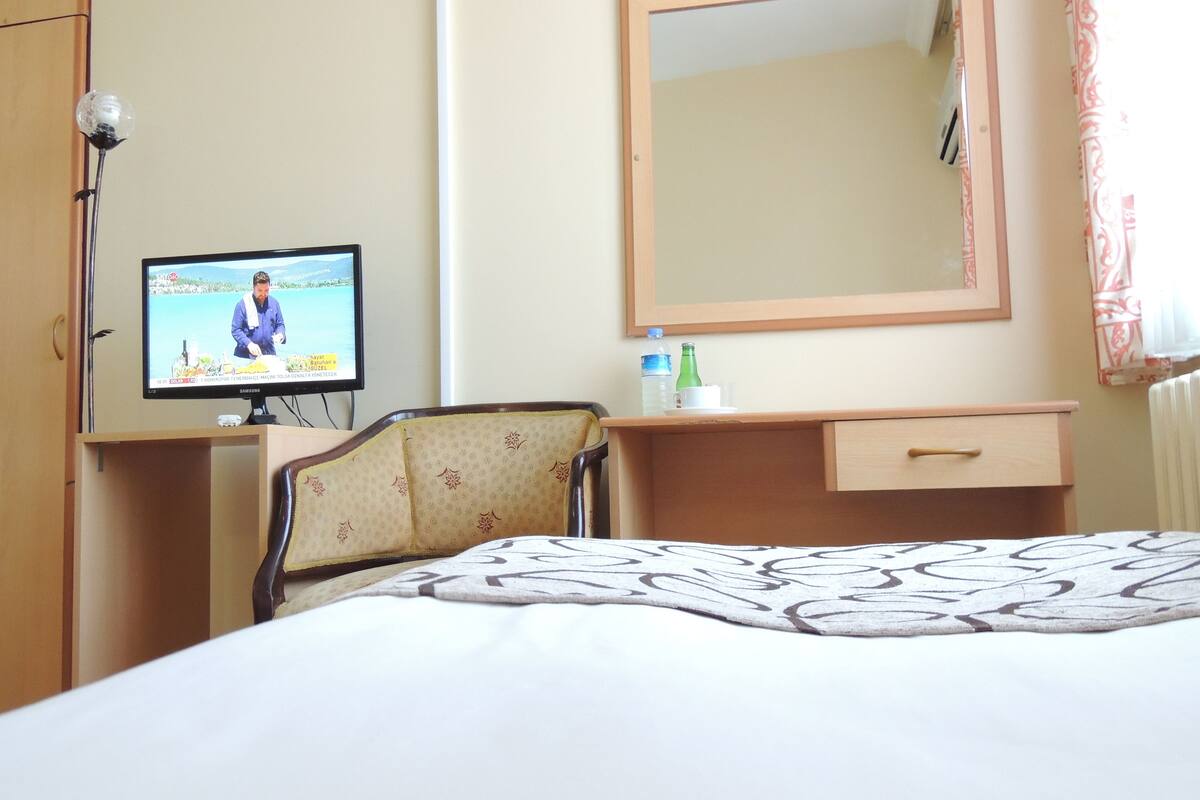 A hotel room with a bed, a desk with a television, a chair, a mirror, and a dresser.