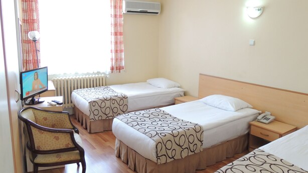 A hotel room with two beds, a chair, a TV, and a bedside table with a phone. - Acikgoz Hotel (Edirne)