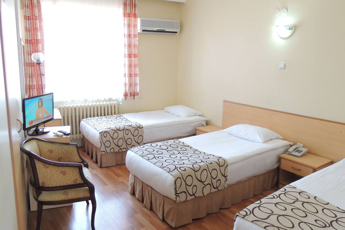 A hotel room with two beds, a chair, a TV, and a bedside table with a phone.