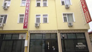 A hotel building with multiple windows and air conditioning units. The building has a yellow facade and a red sign with the hotel's name. - Acikgoz Hotel (Edirne)