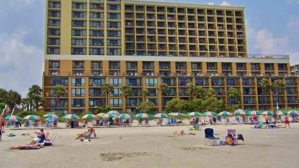 Un hôtel à plusieurs étages, situé en bord de plage et doté de parasols.
