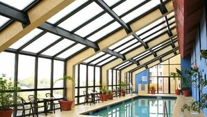 Une piscine intérieure dotée d’un toit en verre, entourée de plantes en pot et d’espaces aménagés pour s’asseoir.