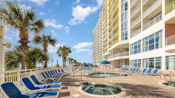 A pool area with lounge chairs, a water feature, and a tall building with balconies.