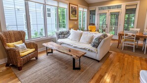 Una sala de estar acogedora con un sillón de mimbre, un sofá blanco, una mesa de centro de madera y una zona de comedor con mesa y sillas.