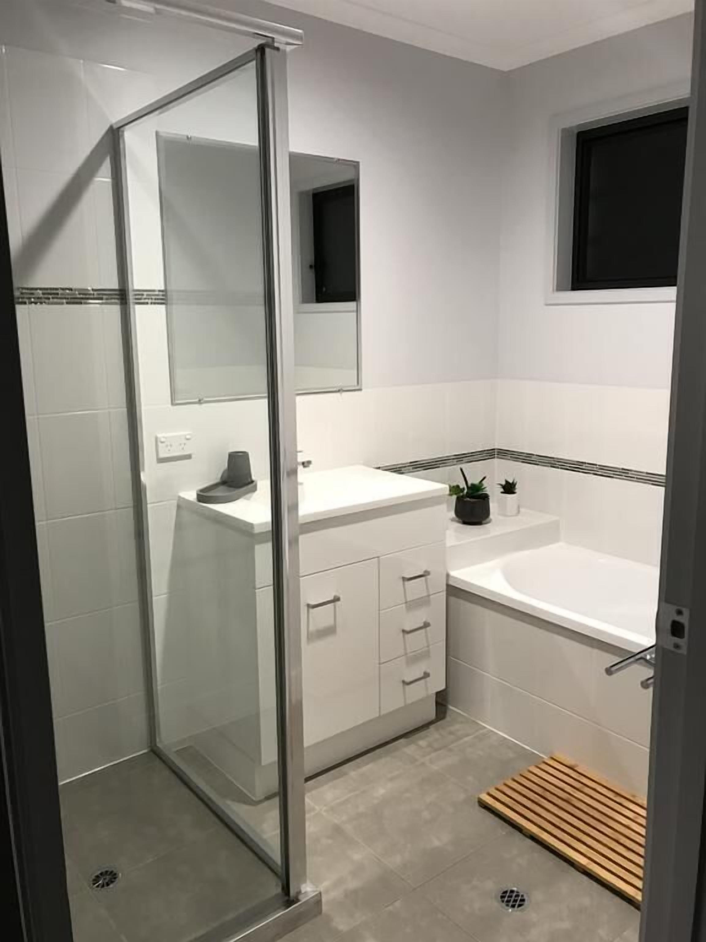 Un baño moderno con cabina de ducha de vidrio, un lavabo blanco, una bañera y una ventana pequeña.
